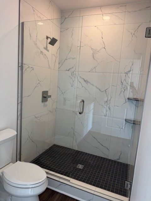 full bath with a marble finish shower and toilet