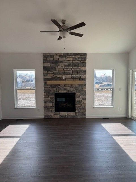 unfurnished living room with ceiling fan, baseboards, wood finished floors, and a stone fireplace