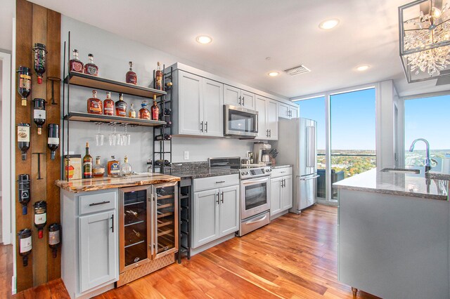 kitchen featuring sink, wine cooler, light stone counters, light hardwood / wood-style flooring, and appliances with stainless steel finishes