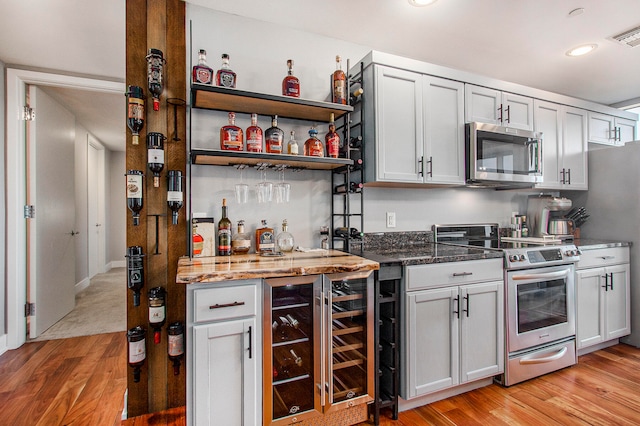 kitchen featuring stone counters, beverage cooler, light wood-type flooring, and appliances with stainless steel finishes