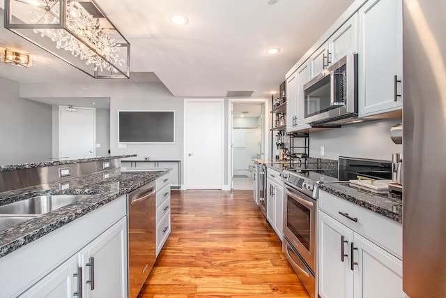 kitchen featuring stainless steel appliances, light hardwood / wood-style flooring, dark stone countertops, white cabinets, and a chandelier