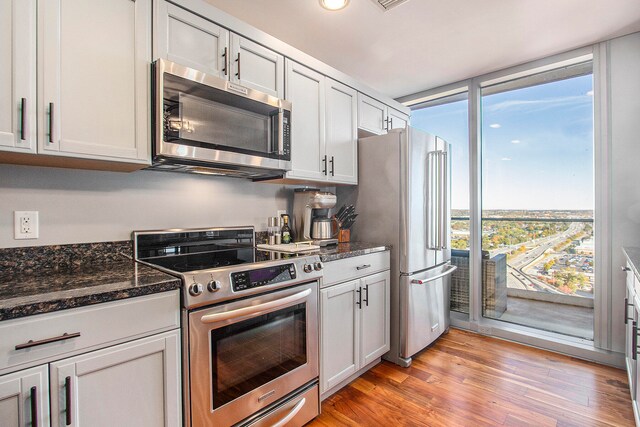 kitchen with light hardwood / wood-style floors, high quality appliances, white cabinetry, and dark stone counters