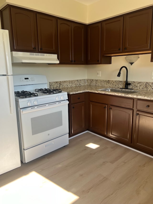 kitchen with light stone countertops, sink, white appliances, and light wood-type flooring