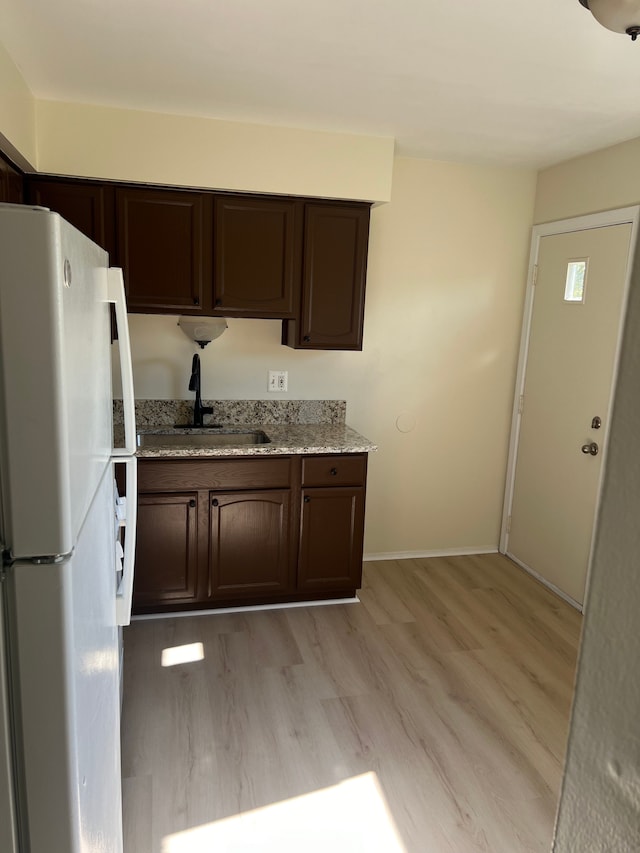 kitchen featuring sink, light hardwood / wood-style flooring, white fridge, light stone counters, and dark brown cabinetry