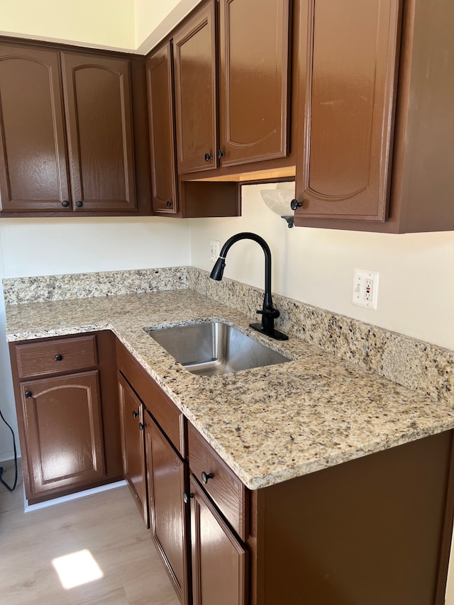 kitchen featuring dark brown cabinets, light hardwood / wood-style floors, light stone counters, and sink