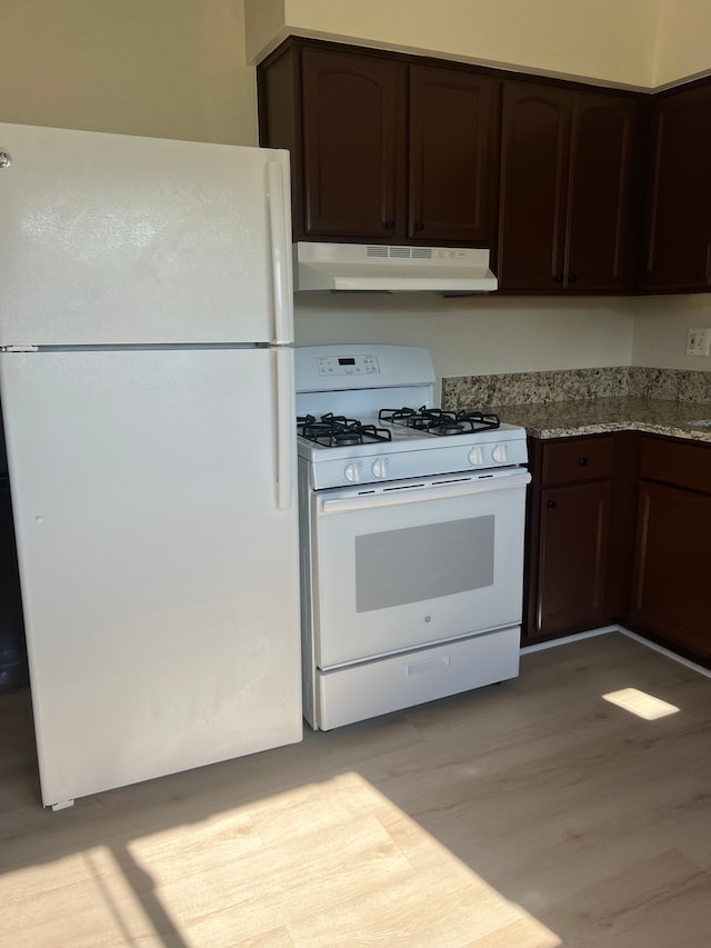 kitchen featuring light stone countertops, dark brown cabinets, light wood-type flooring, and white appliances