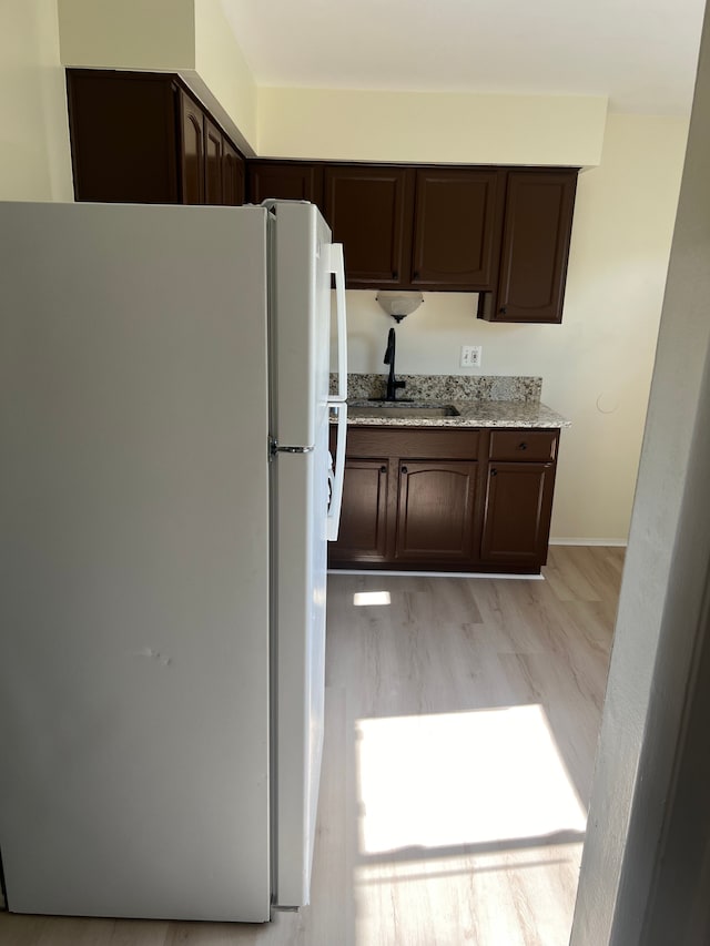 kitchen featuring dark brown cabinetry, light stone countertops, sink, white refrigerator, and light wood-type flooring