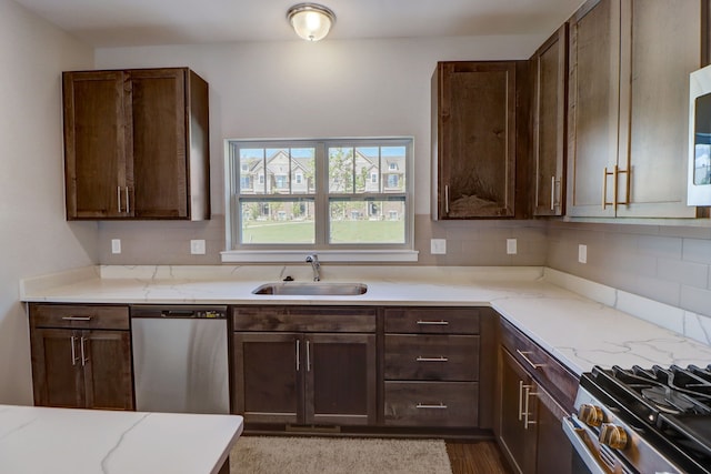 kitchen featuring light stone countertops, decorative backsplash, stainless steel dishwasher, dark brown cabinetry, and sink