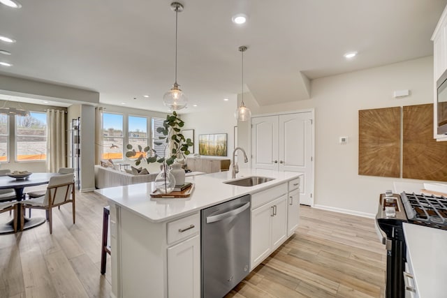 kitchen featuring stainless steel appliances, a sink, white cabinets, light countertops, and an island with sink