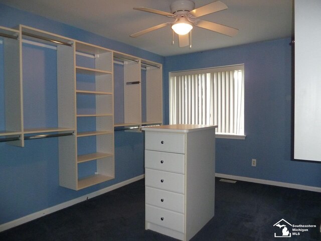 spacious closet with dark colored carpet and ceiling fan