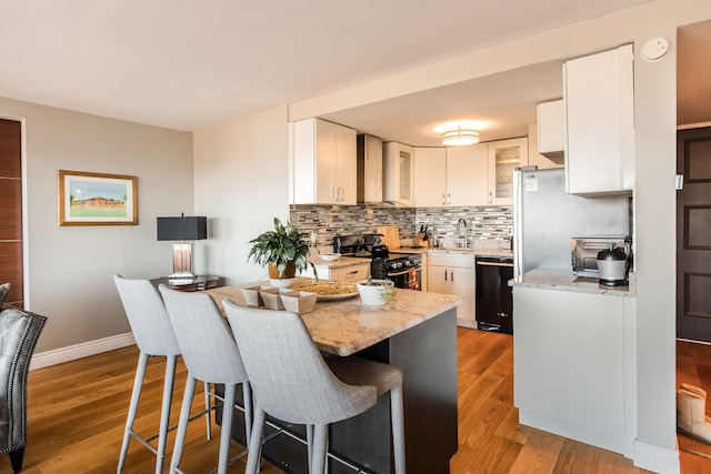 kitchen with white cabinetry, black appliances, wall chimney range hood, and wood-type flooring