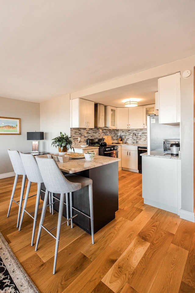 kitchen featuring backsplash, black appliances, a kitchen breakfast bar, light hardwood / wood-style flooring, and white cabinetry