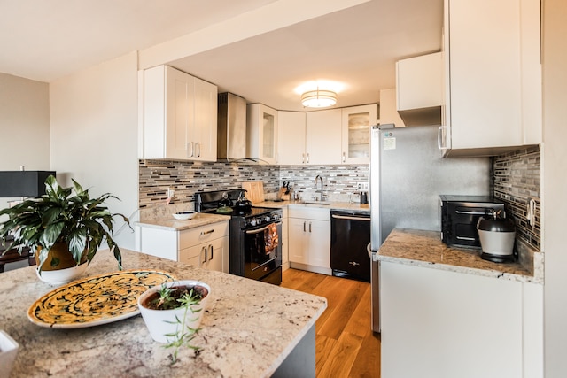 kitchen featuring tasteful backsplash, black appliances, wall chimney range hood, white cabinets, and light hardwood / wood-style floors