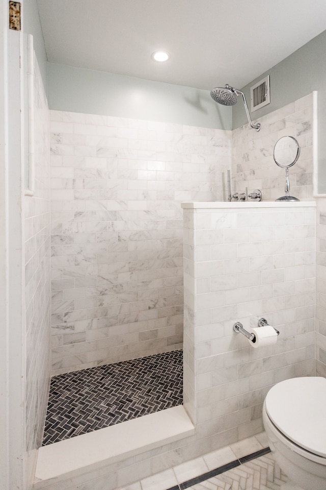 bathroom featuring tile patterned flooring, a tile shower, and toilet