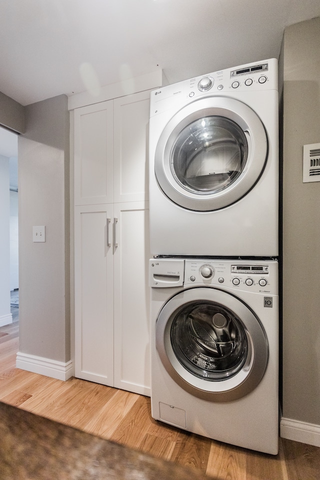 laundry area with cabinets, light wood-type flooring, and stacked washer and dryer