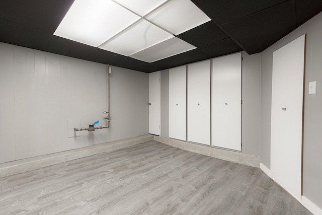 basement featuring a drop ceiling and light hardwood / wood-style floors