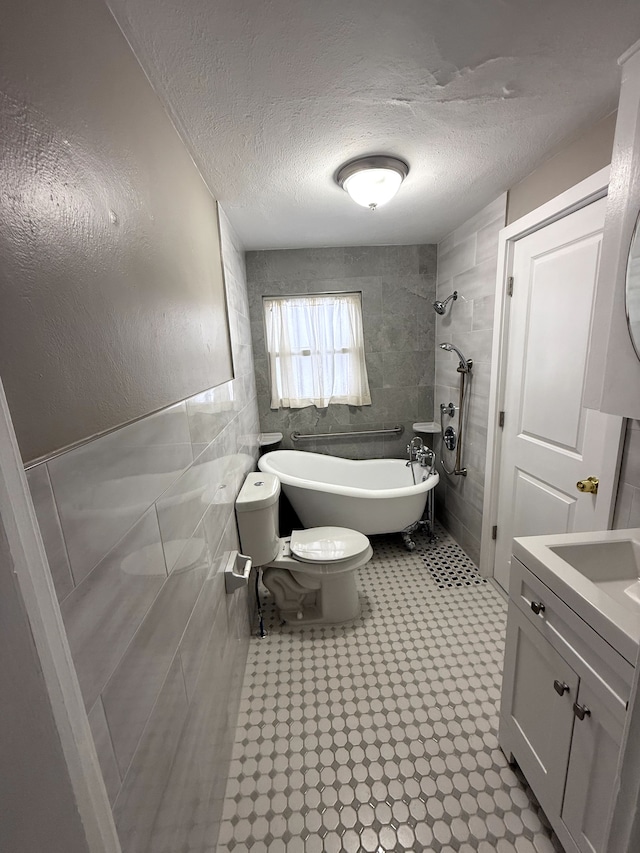 bathroom with a tub to relax in, a textured ceiling, toilet, vanity, and tile walls