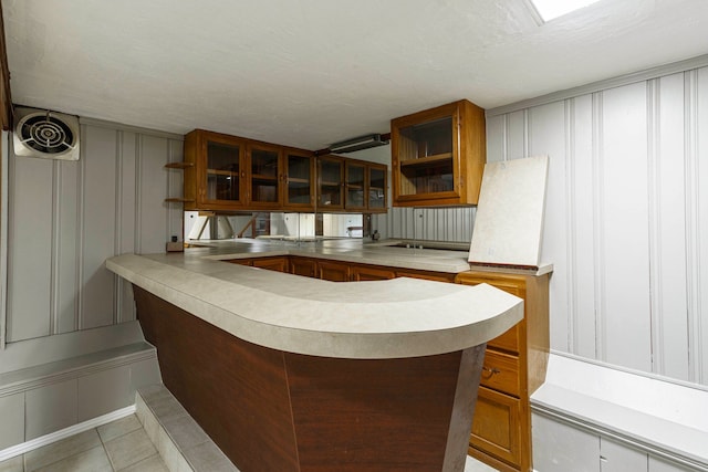 5721 Corunna Ave, Clarkston, MI 48346 - kitchen with a decorative wall, light countertops, glass insert cabinets, brown cabinetry, and a peninsula