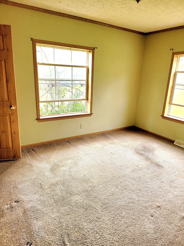 empty room with carpet floors, visible vents, ornamental molding, a textured ceiling, and baseboards