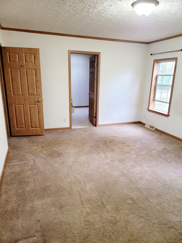 empty room featuring visible vents, ornamental molding, carpet flooring, a textured ceiling, and baseboards