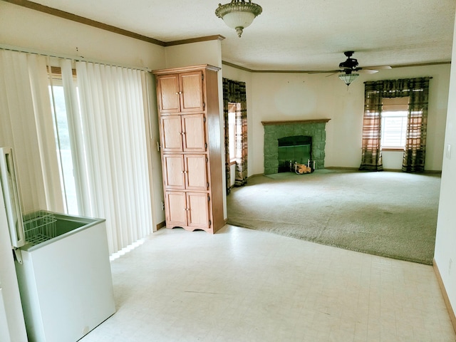 unfurnished living room with light colored carpet, ceiling fan, ornamental molding, a stone fireplace, and light floors