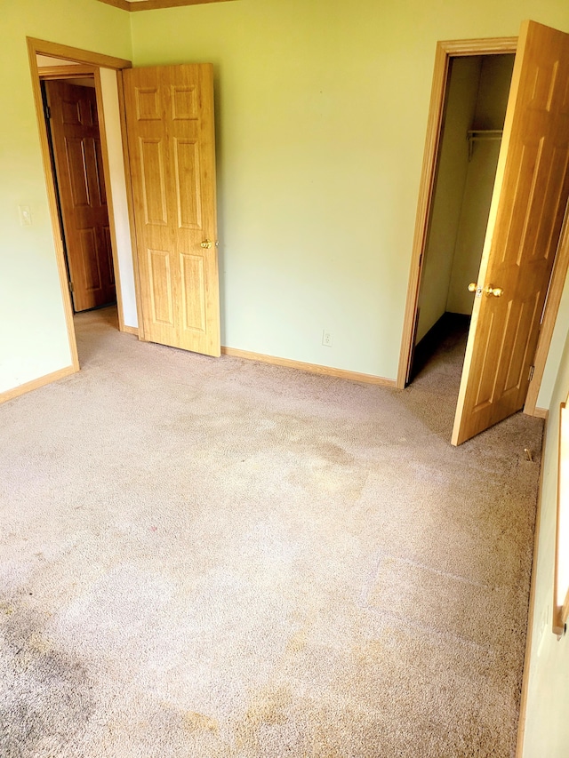 unfurnished bedroom featuring carpet floors, a spacious closet, a closet, and baseboards