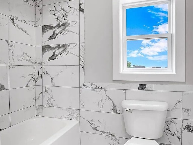 bathroom with tile walls, a bathtub, and toilet