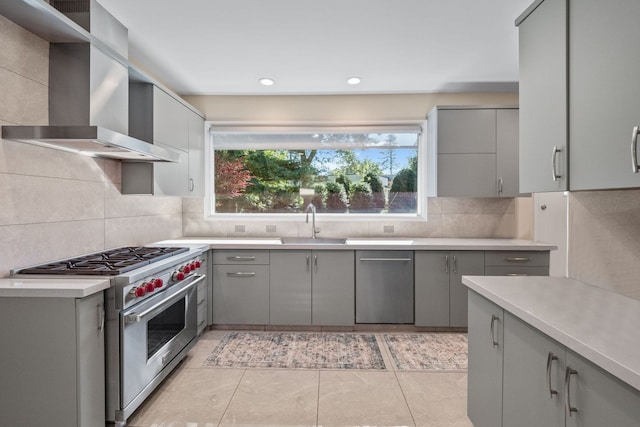 kitchen featuring gray cabinetry, sink, wall chimney range hood, light tile patterned floors, and designer stove