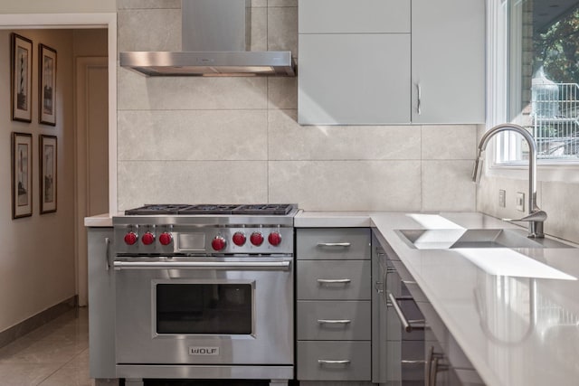 kitchen with gray cabinetry, wall chimney range hood, sink, luxury range, and decorative backsplash