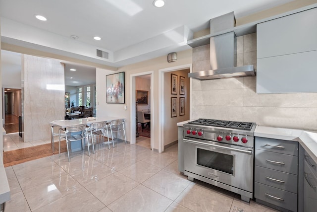 kitchen featuring gray cabinets, premium stove, wall chimney range hood, and tile walls