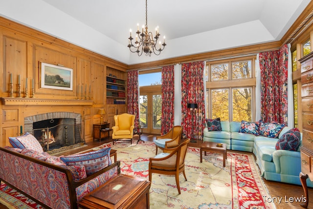 living room featuring wood walls, a brick fireplace, hardwood / wood-style flooring, built in shelves, and a chandelier