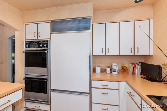 kitchen with black electric stovetop, white cabinetry, double oven, and fridge