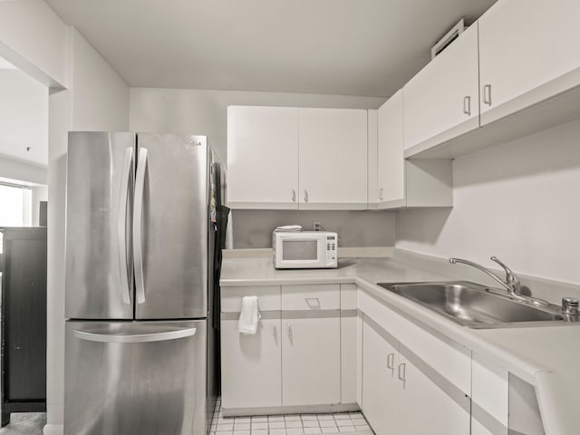 kitchen with stainless steel fridge, white cabinetry, sink, and light tile patterned floors