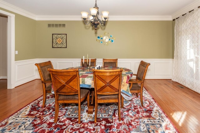 dining space with wood-type flooring, crown molding, and a notable chandelier