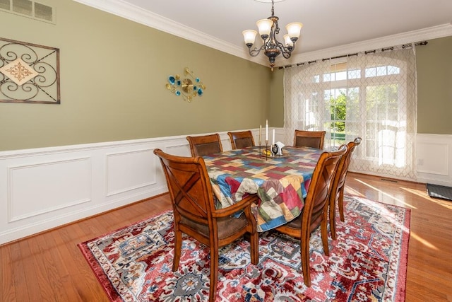 dining area with hardwood / wood-style floors, ornamental molding, and an inviting chandelier