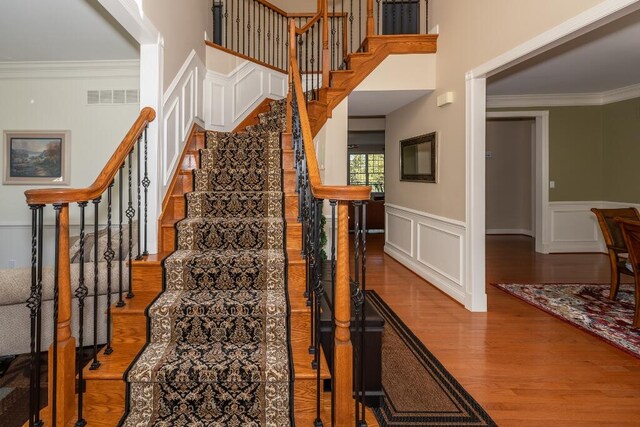 stairs featuring wood-type flooring, ornamental molding, and a high ceiling