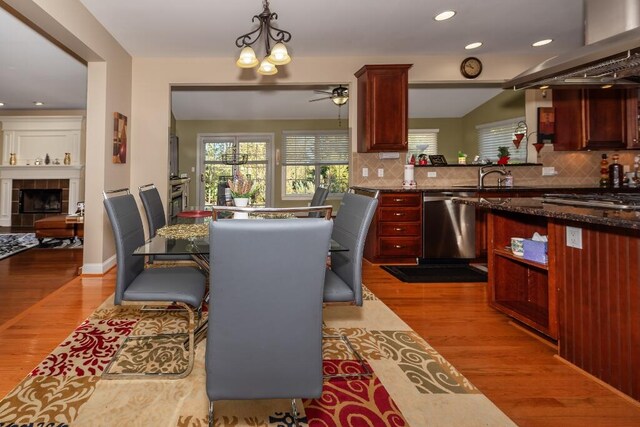 dining space with a fireplace, ceiling fan with notable chandelier, light hardwood / wood-style flooring, and sink