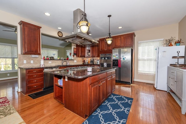 kitchen featuring a center island, hanging light fixtures, dark stone countertops, appliances with stainless steel finishes, and light hardwood / wood-style floors