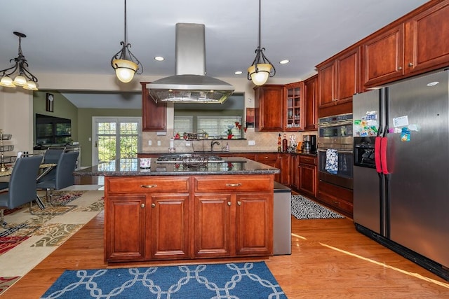 kitchen featuring decorative light fixtures, island range hood, appliances with stainless steel finishes, and light hardwood / wood-style flooring