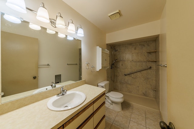 bathroom with tile patterned flooring, vanity, tiled shower, and toilet