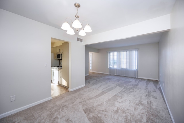 empty room with light colored carpet and a chandelier