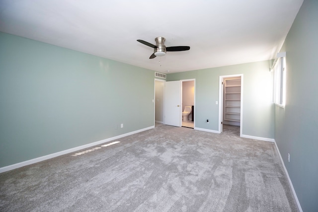 unfurnished bedroom featuring ceiling fan, a spacious closet, connected bathroom, light colored carpet, and a closet