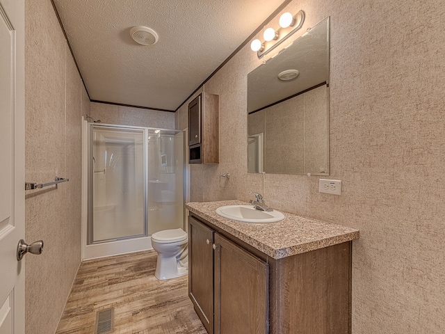 bathroom with hardwood / wood-style floors, vanity, toilet, a textured ceiling, and a shower with shower door