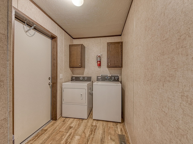 washroom with cabinets, crown molding, light hardwood / wood-style flooring, washing machine and dryer, and a textured ceiling