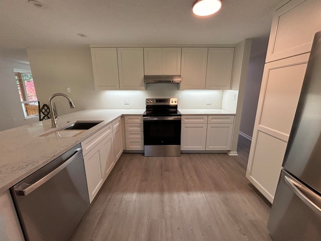 kitchen with kitchen peninsula, appliances with stainless steel finishes, sink, light hardwood / wood-style flooring, and white cabinetry