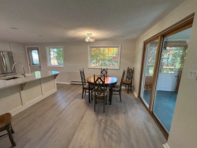 dining room featuring a textured ceiling, wood-type flooring, sink, and baseboard heating