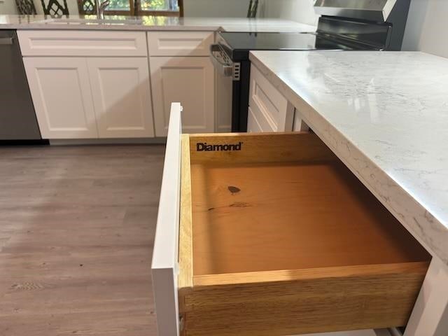 kitchen with dishwasher, black range oven, white cabinets, sink, and light wood-type flooring