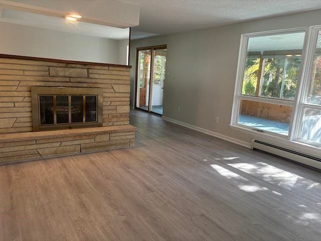 unfurnished living room featuring a stone fireplace, hardwood / wood-style floors, a baseboard radiator, and a textured ceiling