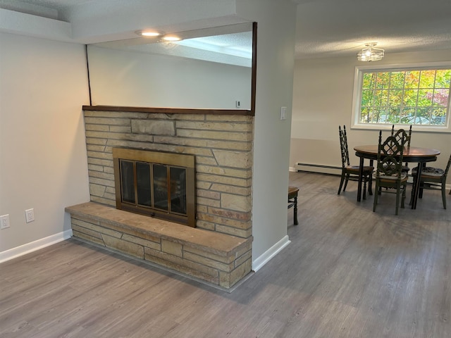 living room featuring baseboard heating, a fireplace, hardwood / wood-style floors, and a textured ceiling