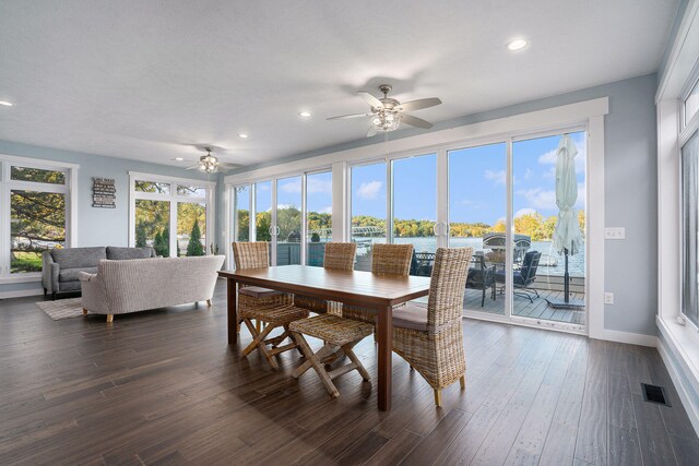 dining space with a water view, a wealth of natural light, dark wood-type flooring, and ceiling fan